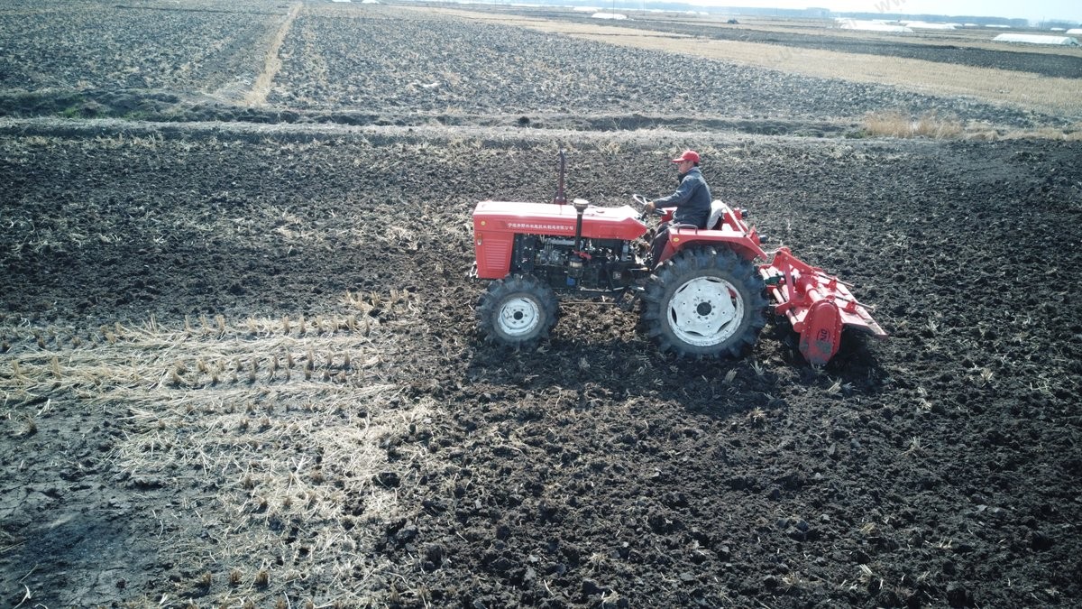 Tractor with rotary tiller working a paddy field, aerial view